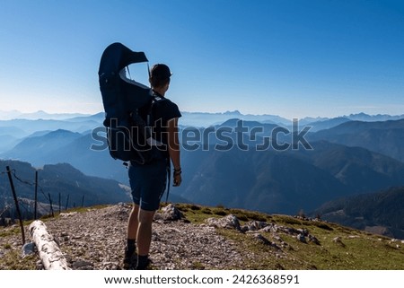 Man with baby carrier looking at magical mountain peaks of Karawanks and Julian Alps seen from Goldeck, Latschur group, Gailtal Alps, Carintha, Austria. Mystical atmosphere in Austrian Alps in summer Royalty-Free Stock Photo #2426368591