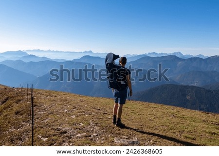 Man with baby carrier looking at magical mountain peaks of Karawanks and Julian Alps seen from Goldeck, Latschur group, Gailtal Alps, Carintha, Austria. Mystical atmosphere in Austrian Alps in summer Royalty-Free Stock Photo #2426368605
