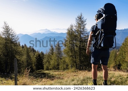Man with baby carrier looking at magical mountain peaks of Karawanks and Julian Alps seen from Goldeck, Latschur group, Gailtal Alps, Carintha, Austria. Mystical atmosphere in Austrian Alps in summer Royalty-Free Stock Photo #2426368623