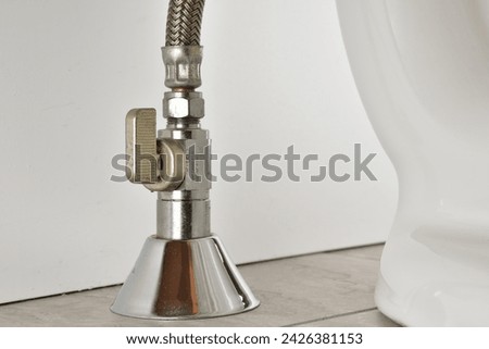 Toilet water feed line. Water valve on toilet inlet with braided hose. Ball valve vertical installation with water line coming from the floor. Toilet installation. Royalty-Free Stock Photo #2426381153