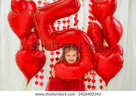 A frisky naughty child with a big red ballon in the shape of the number five shows his tongue. The first mini anniversary of the child Royalty-Free Stock Photo #2426402243