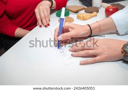 dietitian and young girl who wants to lose weight examines the information sheet. nutrition and diet specialist prescribes a prescription to a patient who comes to lose weight. healthy living concept Royalty-Free Stock Photo #2426405051