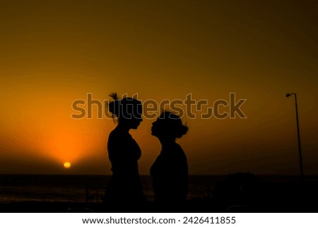 portrait of two women looking at each other face to face on the seashore in a romantic sunset