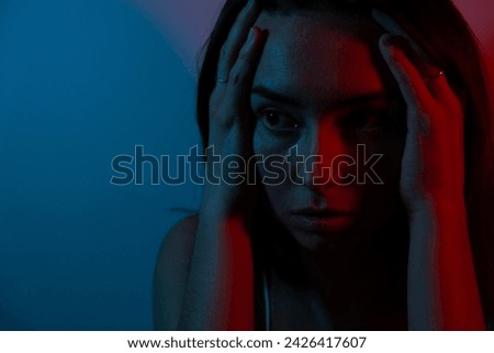 Emotional photo. Blue and red colors. Portrait photo of a woman. A young woman feels stressed and anxious.
Sad woman complaining alone sitting in the dark.Depressed young woman coping with loss, grief