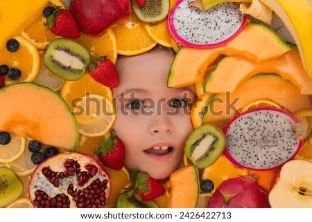 Funny fruits. Kids face with mix of strawberry, blueberry, strawberry, kiwi, dragon fruit, pomegranate, orange and melon. Assorted mix of fruits near child face.