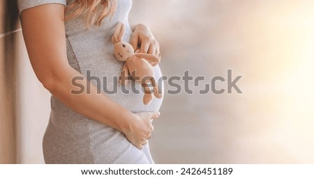 Close up of a pregnant blonde womans belly, who's holding cute baby bunny toy next to her tummy