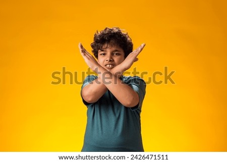 Portrait of child boy showing stop gesture on yellow background. Bulling and negative emotions concept