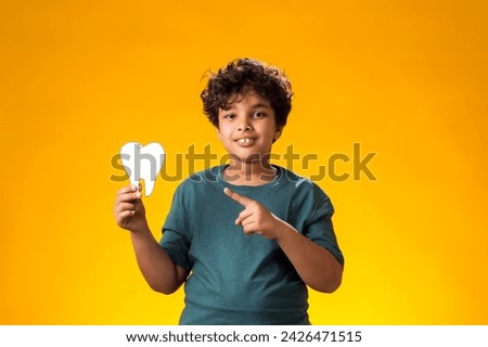 Portrait of child boy holding papercraft tooth and pointing finger at it over yellow background. Dental health concept