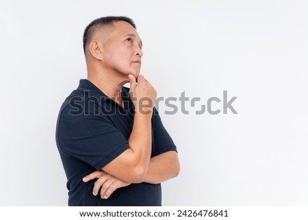 Side view of a contemplative middle-aged Asian man looking upwards, hand on chin, isolated over a white background, pondering. Royalty-Free Stock Photo #2426476841