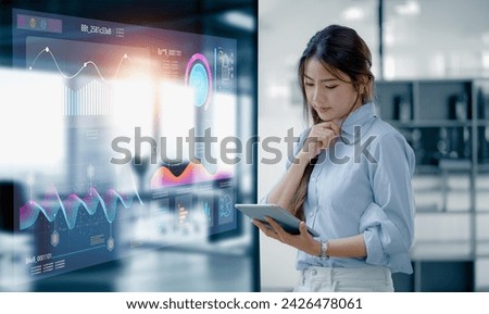 Happy asian young businesswoman using digital tablet with business finance chart dashboard on virtual screen and standing in office  working space, Business finance data analytics and market concept. Royalty-Free Stock Photo #2426478061