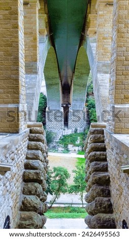 Symmetrical view under a bridge, showcasing architectural columns and an arched ceiling, with vegetation visible at the far end.
