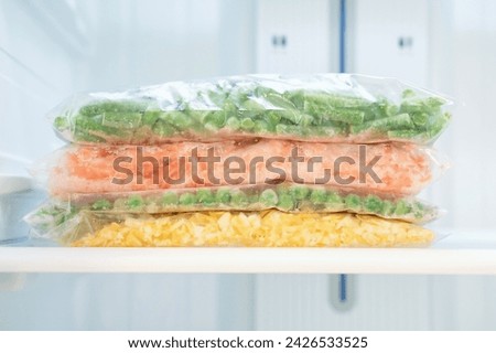 Frozen vegetables in a plastic bags in freezer close up, front view.