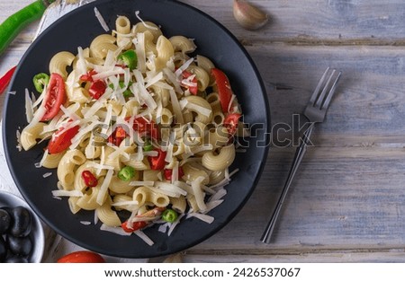 Italian pasta with cherry tomatoes, peppers and grated parmesan cheese in a black plate and on a wooden table.