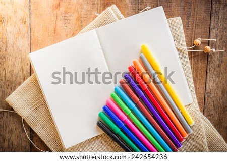 Blank notebook with many color markers on wooden table. The view from the top