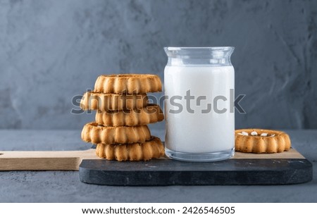 Milk in a glass container with biscuits on a board and on a concrete table.