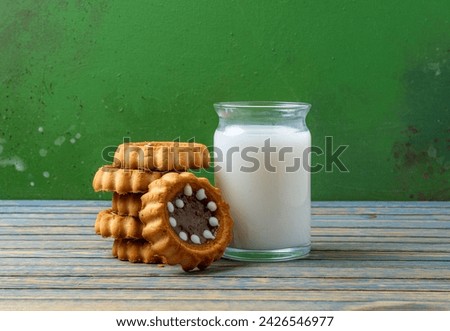 Milk in a glass container with biscuits on a wooden table.