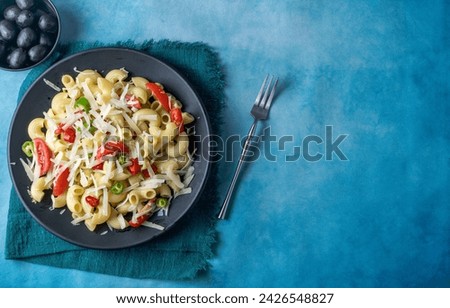 Italian pasta with cherry tomatoes, peppers and grated Parmesan cheese in a black plate. Top view with space for text.
