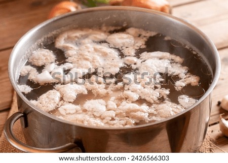 Removing the white foam know as chicken scum from the surface of stock pot when boiling chicken. Bone broth