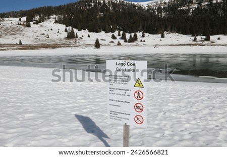Warning sign on the shore of Coe Lake in Northern Italy in winter with snow
