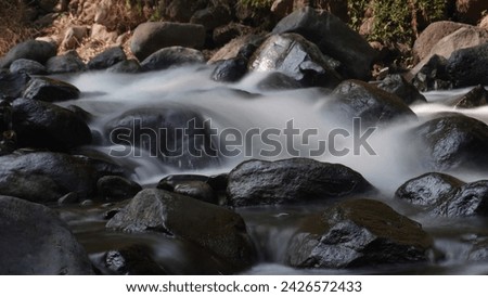 In the photo there is a waterfall located in the forest, and there are various objects consisting of rocks, water which becomes cotton. The shooting technique uses a low shutter speed