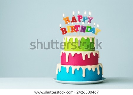 Colorful tiered birthday cake with colorful happy birthday candles and drip icing Royalty-Free Stock Photo #2426580467