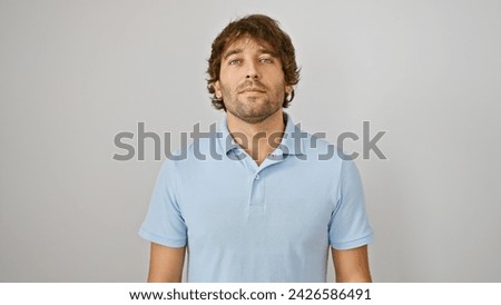 A handsome caucasian man with a beard in a blue shirt stands against a white isolated background, exuding casual confidence. Royalty-Free Stock Photo #2426586491