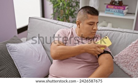 Confident latin guy, scanning his diabetes sensor with phone, monitoring glucose levels at home, serious yet relaxed Royalty-Free Stock Photo #2426587675