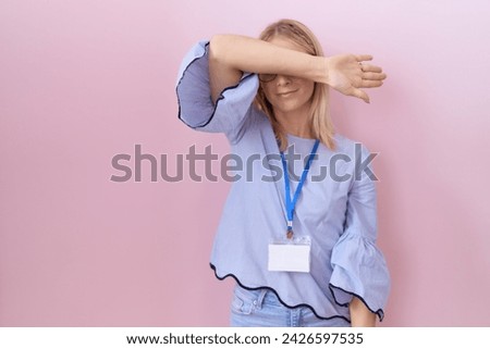 Young caucasian business woman wearing id card covering eyes with arm, looking serious and sad. sightless, hiding and rejection concept  Royalty-Free Stock Photo #2426597535