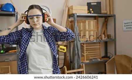 Caucasian woman wearing safety gear in a carpentry workshop surrounded by wooden furniture and tools.