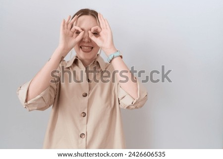 Young caucasian woman wearing casual shirt doing ok gesture like binoculars sticking tongue out, eyes looking through fingers. crazy expression. 