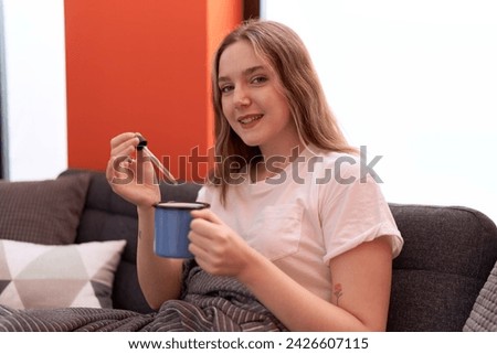 Young caucasian woman drinking coffee sitting on sofa at home