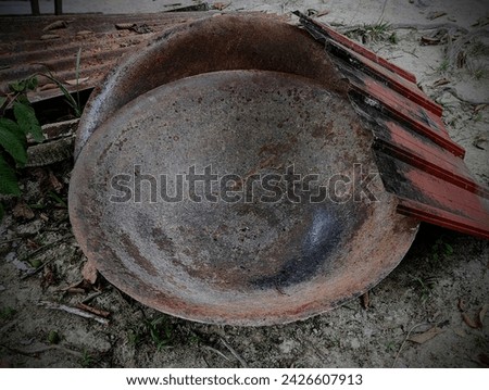 A picture of two very large pots. At the edges there is one old zinc sheet .This large pan is used for cooking during feasts by the community in the village in the state, Kedah.