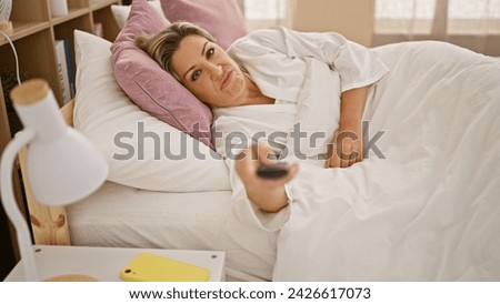 Young blonde woman watching tv lying on bed tired at bedroom