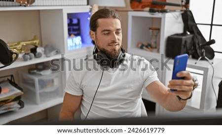 Young hispanic man wearing headphone make selfie picture by camera at music studio