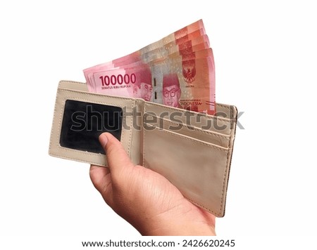 Hand holding a wallet containing several Indonesian rupiah notes.  The concept of bonus money or THR, rupiah money is given during the month of Ramadan.  Isolated on white background Royalty-Free Stock Photo #2426620245