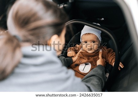 Rear view of unrecognizable young mom placing child safety seat with infant baby boy on back passenger seat. Concept of safety lifestyle, driving and travel. Royalty-Free Stock Photo #2426635017