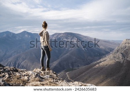 Hiker girl on the mountain top in trip, sport and active life concept, young girl enjoying view on peak of sunny mountain, tourist traveler on background view mockup  Royalty-Free Stock Photo #2426635683