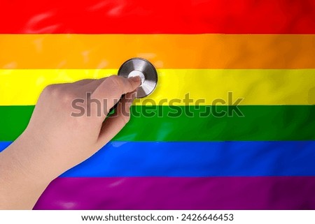 The head of a medical stethoscope in a hand (close-up) against the background of a rainbow flag (LGBT). LGBT healthcare. Treatment and rights for gays, lesbians, bisexuals and transgender people