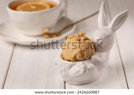 A ball of natural craft lemon ice cream with pine nuts. A serving figurine of the Easter bunny. A cup of tea with lemon