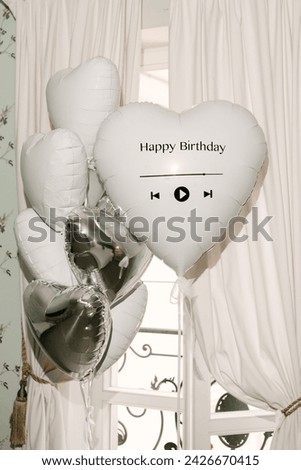 A set of helium balloons with foil white and silver hearts with the inscription happy birthday in a beautiful interior