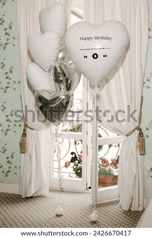 A set of helium balloons with foil white and silver hearts with the inscription happy birthday in a beautiful interior