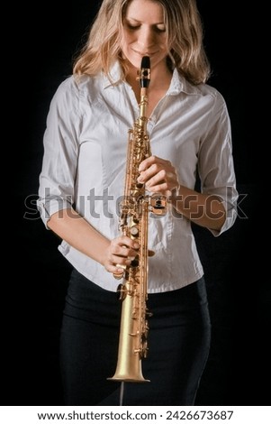 soprano saxophone in the hands of a girl on a black background Royalty-Free Stock Photo #2426673687