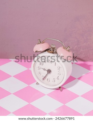 Vintage alarm bell clock in stylized pink checkered background, retro nostalgia, oldies greatest hits playlist.
