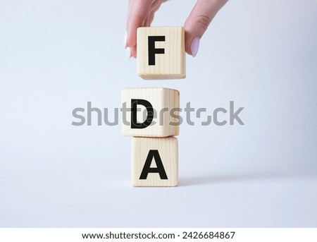 FDA - Food Drug Administration symbol. Wooden cubes with word FDA. Doctor hand. Beautiful white background. Medical and Food Drug Administration concept. Copy space.