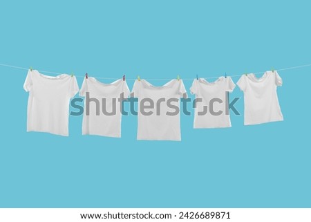 T-shirts drying on washing line against light blue background Royalty-Free Stock Photo #2426689871