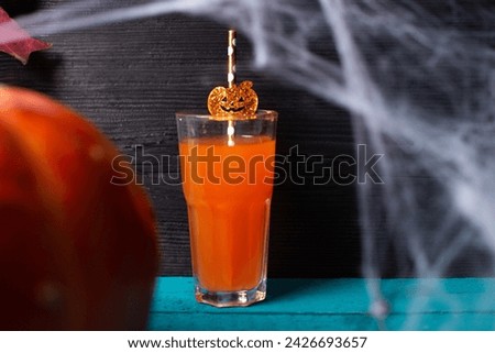 A glass of juice with a pumpkin and a spider web for Halloween