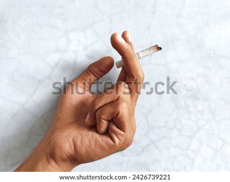 A man's hand holding a cigarette in the middle of a white wall with cracked paint.