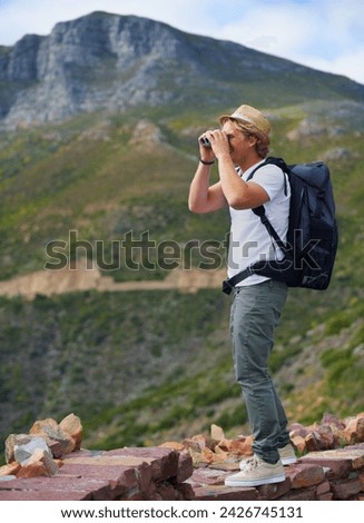 Man, traveler and binoculars with backpack for sightseeing, outdoor travel or hiking on mountain in nature Young male person, hiker or tourist with bag or optical instrument for view, vision or scope Royalty-Free Stock Photo #2426745131