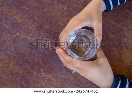 Top view a hand catching glass of pure water on the wooden table, healthcare and refreshment concept, copy space for text