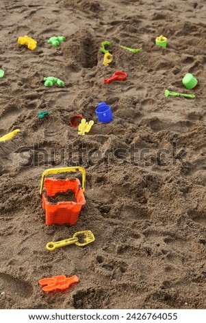 Exterior photo view of a kid sand playground with many plastic toys for playing at the beach like shovel bucket animals molds dispatched randomly outdoor